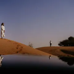 A surreal and artistic photograph in the Abu Dhabi desert, using a water reflection to create a stunning mirage effect. This shot highlights our creative approach to landscape and destination couple photography.