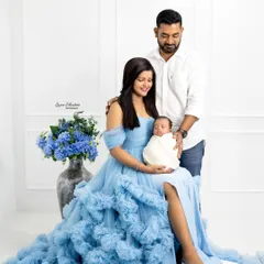 A beautiful family portrait featuring a mother in a stunning blue gown, holding her newborn alongside her partner. This showcases a more formal, elegant style of family photography.