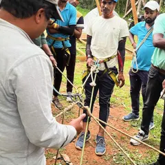 A participant learns the intricacies of a friction hitch during a knot-tying session. This practical skill is crucial for self-rescue and advanced rope work, taught under close supervision.