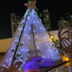 A wider shot of the butterfly-themed teepee against the city backdrop at night. The cool-toned fairy lights and purple cushions tie back to the main lavender theme of the party, creating a cohesive look.