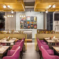 A view of the booth seating at Pasta Street, separated by low planters that add a touch of green. In the background, a gallery wall of framed prints and our custom-made rectangular lights create layers of visual interest.