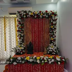 This floral frame setup, while often used for poojas, can also be adapted for a respectful memorial service. The arrangement uses a mix of red, yellow, and white flowers.