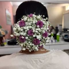 A full, round bridal bun completely covered in a mix of baby's breath and tiny purple flowers. This creates a lush, garden-like effect that is both romantic and eye-catching.