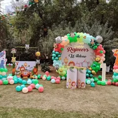 An outdoor "Wild One" birthday party with a jungle theme. The setup includes a personalized backdrop, various animal cutouts, and a colorful balloon garland scattered on the lawn.