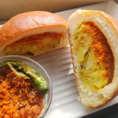 A perfect cross-section of the Baked Vada Pav, showing the generous potato filling and chutney inside the soft, golden-brown bun.