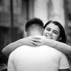 A hug is a simple gesture full of meaning. This candid, over-the-shoulder shot captures the bride-to-be's joyful smile, showing a moment of pure happiness and comfort during their pre-wedding shoot.