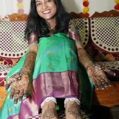 A happy bride showing her complete mehendi look, with beautiful, matching designs on her hands and feet.