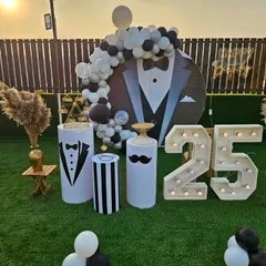 A dapper "tuxedo" themed 25th birthday party. This outdoor setup features a suit-and-tie backdrop, marquee numbers, and fun details like a mustache prop.