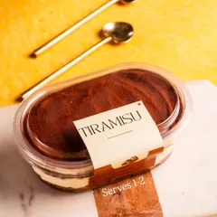 A stylish shot of our Tiramisu tub, ready to be enjoyed with two golden spoons. It's the perfect shareable personal dessert.