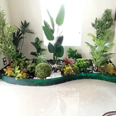 A custom-designed curved planter for a home interior, filled with a diverse mix of artificial plants, rocks, and a central moss ball. This unique piece is designed to fit perfectly in an unused corner.