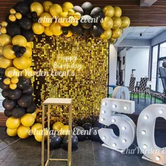 This 50th birthday setup uses large white marquee numbers for a clean, modern look against a bold black, yellow, and gold sequin background.