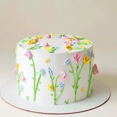 A minimalist cake decorated with delicate, hand-piped wildflowers. The simple white background makes the pastel-colored buttercream flowers stand out, creating a fresh, garden-like feel.