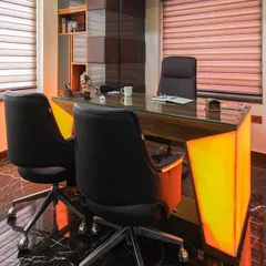A finished director's room featuring a custom desk with an illuminated onyx front. The design combines glossy black marble floors with rich wood veneer storage, creating a classic executive look with a modern lighting twist.