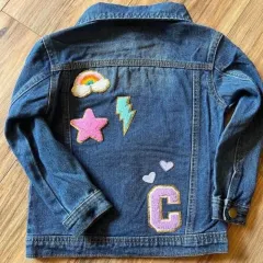 This denim jacket is personalized with the initial "C" and fun patches like a rainbow, star, and lightning bolt.