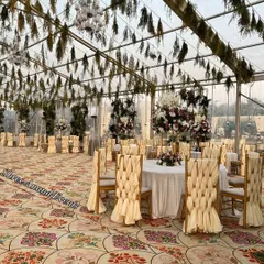 A beautiful indoor-outdoor dining area with a transparent ceiling, featuring chairs with unique woven back covers and a floral-patterned carpet.