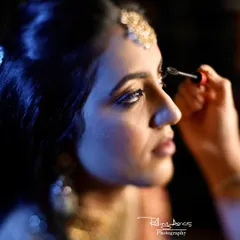 A close-up shot of the bride having her mascara applied. The dramatic blue lighting and focused angle create a cinematic and artistic getting-ready photograph.