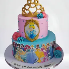 A two-tier Disney princess cake featuring Cinderella and an array of other beloved princesses. This whipped cream cake is decorated with a golden tiara and edible images for a magical 6th birthday.
