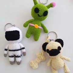 Here are three more examples of my custom crochet keychains. This group features a small astronaut in a white suit, a green alien with pink antennae, and a pug complete with its own tiny crocheted bone.