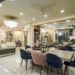 A wide shot of an open-plan home, showing the dining area with jewel-toned chairs flowing into the living room, unified by a large mirrored wall that enhances the sense of space.