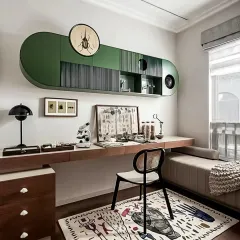 A unique and eclectic study space with custom-designed green overhead cabinets and a long wooden desk. The space is personalized with interesting art and a patterned rug.