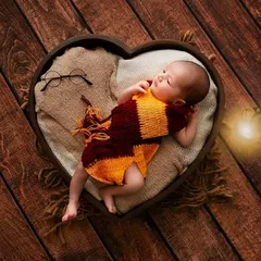 A newborn styled as Harry Potter, complete with a Gryffindor scarf and glasses, in a heart-shaped prop.