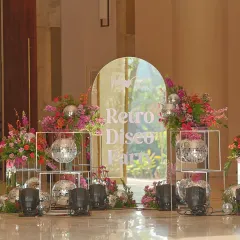 The entrance to the "Retro Disco Party" Mehendi, featuring a mirrored arch with the event's theme, surrounded by disco balls and lush, colorful flowers.
