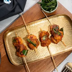 Succulent Ghee Roast Prawns served on satay sticks. This appetizer combines traditional coastal spices with a modern, easy-to-eat presentation.