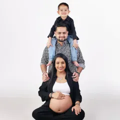 A creative family pose, with the son sitting on his father's shoulders, forming a tower of love above the expecting mother.