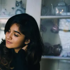 A natural light portrait of a woman looking thoughtfully to the side, with a cabinet of curios in the background. The setting adds a touch of personality and story to this simple, beautiful shot.