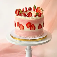 A stunning strawberry cake with pink and white striped buttercream. The cake is decorated with sliced strawberries around the base and topped with a pile of fresh fruit.