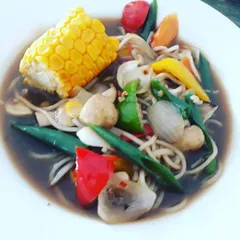 A comforting Chinese-inspired bowl filled with soupy noodles, corn on the cob, and a medley of crunchy vegetables in a savory garlic sauce. It's a one-bowl wonder for a chilly evening.