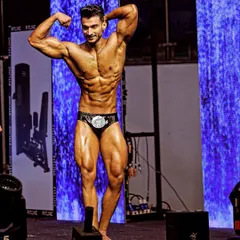 Classic physique posing on the competition stage. This pose highlights the V-taper, shoulder-to-waist ratio, and overall body symmetry we work to perfect.