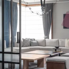 A glimpse into the living room through a sleek, glass-paneled sliding door. This view highlights the open, airy feel of the space, with a focus on modern furniture and a cohesive color palette.