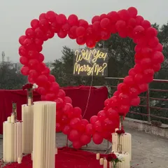 I love creating bold and romantic statements, like this stunning terrace proposal setup. A giant heart-shaped arch made of red balloons creates a dramatic frame for the 'Will You Marry Me?' neon sign, while the red carpet and candles make the moment feel like a movie scene.