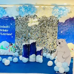A 'Winter ONEDERLAND' theme for a first birthday party. The scene features a custom backdrop, a silver sequin wall, a polar bear cutout, and marquee 'ONE' letters, all tied together with a blue and white balloon arrangement.