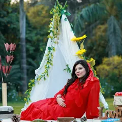 A solo portrait from our outdoor picnic setup. The mom-to-be relaxes on a blanket, surrounded by nature, in a vibrant red dress that beautifully complements the green scenery.