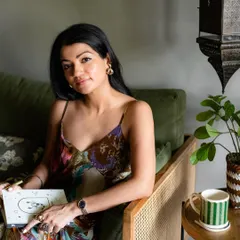 A warm and inviting portrait for Patrika Gift Shop. The model holds a journal, surrounded by cozy home elements like a striped mug and a plant, creating an authentic lifestyle scene.