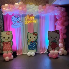 A sweet Hello Kitty theme featuring a pink and white curtain backdrop, a "Happy Birthday" neon sign, and several cute Hello Kitty character cutouts.