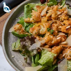 Our roasted cauliflower salad is a warm and hearty option. It features spiced, roasted cauliflower florets on a bed of greens with pine nuts and parmesan shavings.