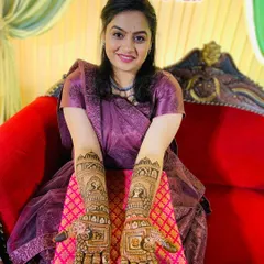 A happy bride showing her detailed wedding mehndi. The design includes personalized initials 'P' and 'R' on the palms, set within a traditional Rajasthani jharokha (window) frame, making it unique to her love story.