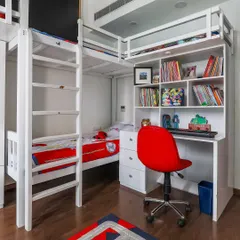 A space-saving solution for a shared kids' room. This custom-built white bunk bed includes an integrated study desk and bookshelf, making it a complete unit for sleep, study, and storage.