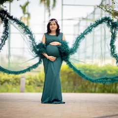 A powerful and dramatic solo portrait. The deep green gown with its wing-like extensions creates a stunning silhouette, celebrating the strength of motherhood.
