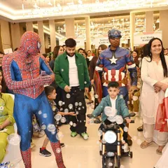 The birthday boy makes a grand entrance on his mini-motorcycle, escorted by Spider-Man and Captain America mascots.
