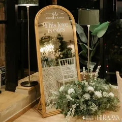We love adding personal, reflective touches to our decor. This elegant arched mirror features a custom decal with the couple's names and the phrase "This love is ours," surrounded by a delicate arrangement of white flowers and greenery.