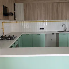 A fresh pistachio green and wood-themed kitchen, featuring a clean white countertop and modern subway tiles. The exposed brass gas pipe adds an industrial touch.