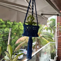 The navy blue planter hanging on a balcony, surrounded by greenery. It's a beautiful and functional piece of macrame art.
