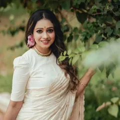 A beautiful Onam portrait. Her direct, engaging gaze and the soft flower in her hair perfectly balance the traditional elegance of the white and gold saree.