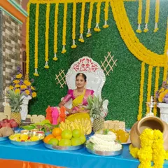 A vibrant half-saree function setup. The backdrop is a green wall decorated with hanging yellow flower garlands, paired with a comfortable throne for the girl of the hour.