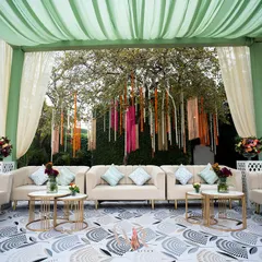 A chic lounge setup for a daytime mehndi. I used a printed floor, plush neutral sofas, and a backdrop of hanging ribbons and florals against a large tree, creating a perfect blend of bohemian elegance and comfort.