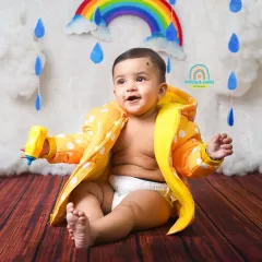 Splish, splash. A happy baby enjoys our monsoon-themed mini-session, complete with a bright yellow raincoat, rainbow, and fluffy clouds.